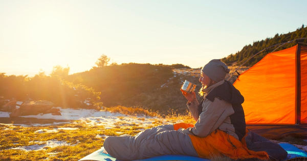 Camper enjoying a morning coffee while sitting in a sleeping bag