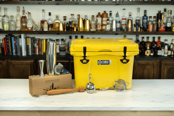 Yellow Cubix rotomolded 25 Quart Viva Cooler displayed on a marble countertop with a craft bar set